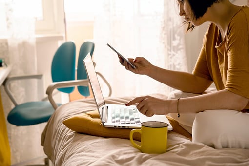 woman doing remote work from bed with laptop and mobile phone woman doing remote work from bed with laptop and mobile phone